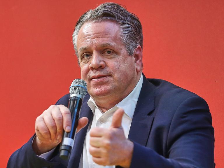 Marcus Bensmann sitzt bei der Leipziger Buchmesse vor einem roten Hintergrund mit einem Mikrofon in der Hand auf einem Podium.