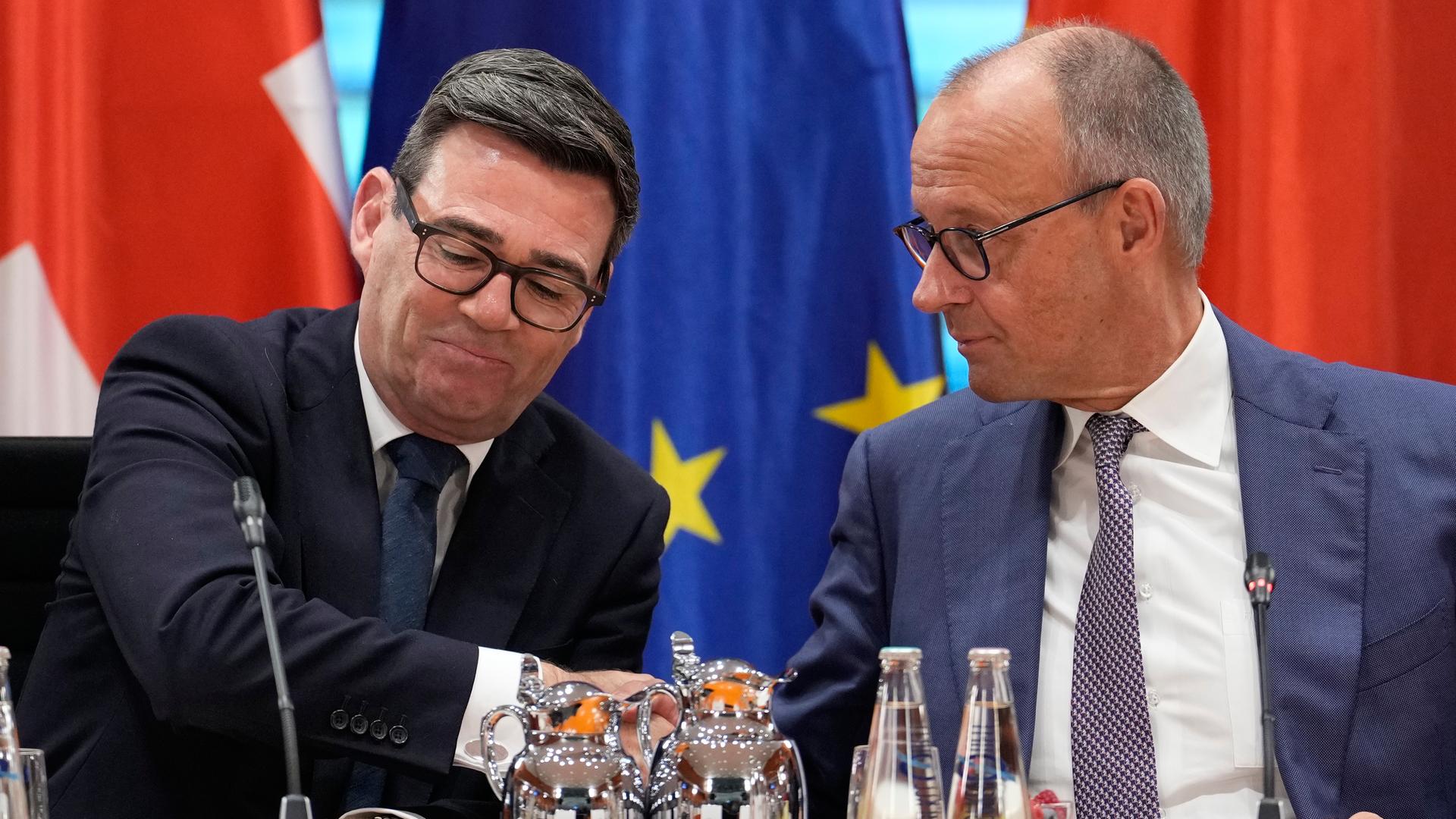 Andy Burnham und Friedrich Merz sitzen nebeneinander. Hinter ihnen sind Fahnen von Großbritannien, Deutschland und der EU. Die beiden Regierungschefs sind zueinander gewandt. Andy Burnham und Friedrich Merz sitzen nebeneinander. Hinter ihnen sind Fahnen von Großbritannien, Deutschland und der EU. Die beiden Regierungschefs sind zueinander gewandt.