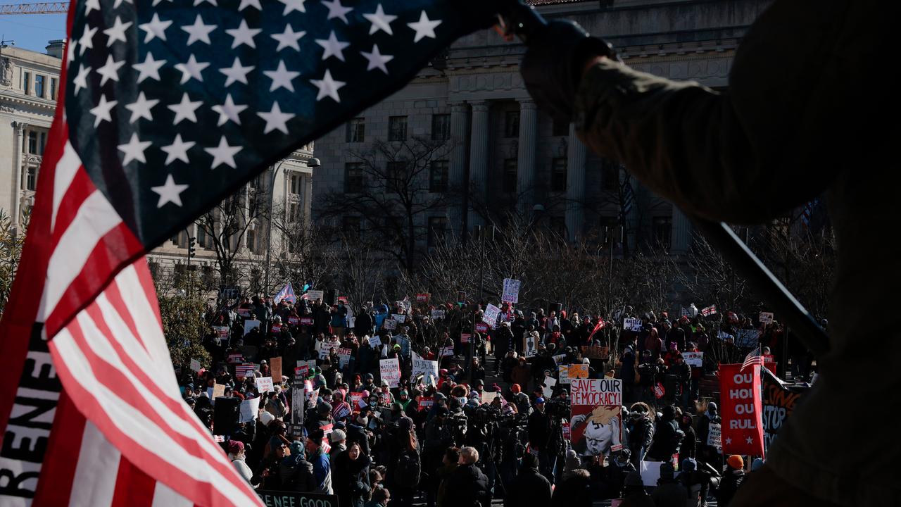 Durch eine verkehrt herum gehaltene Flagge der UA hindurch sind auf einem Platz versammelte Demonstranten zu sehen.