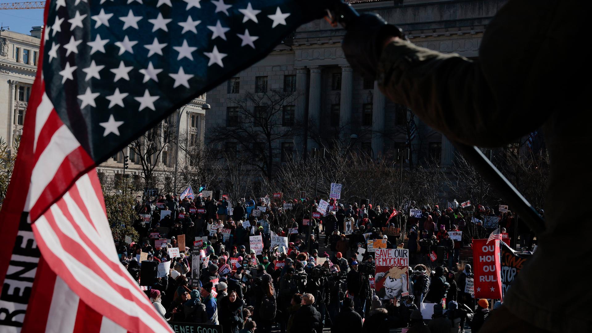 Durch eine verkehrt herum gehaltene Flagge der UA hindurch sind auf einem Platz versammelte Demonstranten zu sehen.