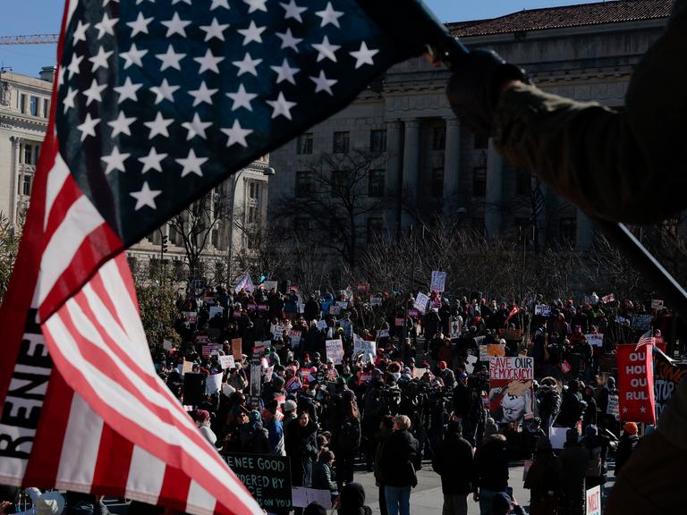 Durch eine verkehrt herum gehaltene Flagge der UA hindurch sind auf einem Platz versammelte Demonstranten zu sehen.