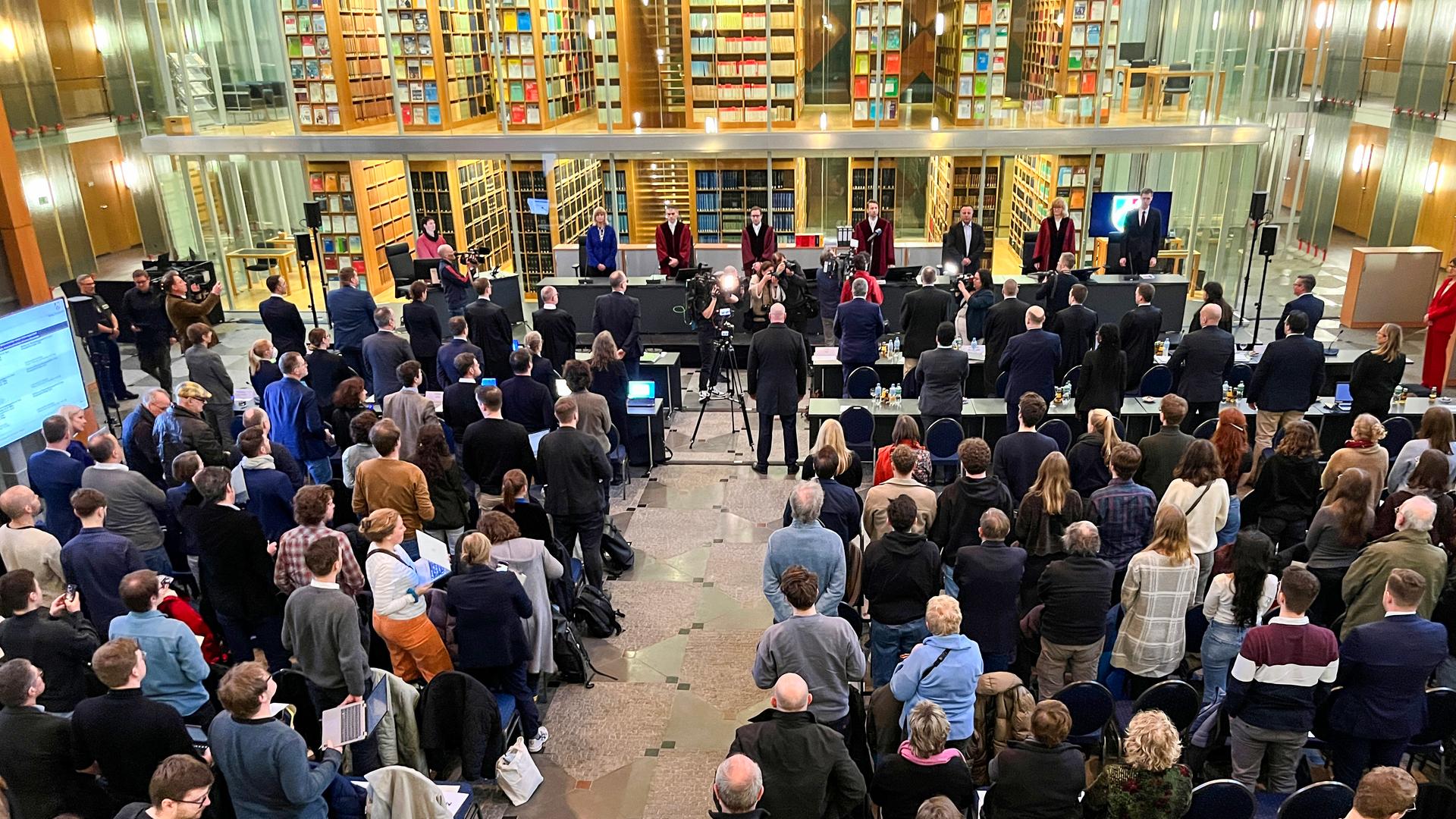 Blick von Hinten in den Saal des Oberlandesgerichts in Münster, in dem das Verfahren gegen die AfD gerade beginnt. Die Zuschauer stehen noch auf ihren Plätzen. Im Hintergrund durch Glasscheiben sind hohe Bücherwände zu sehen. Blick von Hinten in den Saal des Oberlandesgerichts in Münster, in dem das Verfahren gegen die AfD gerade beginnt. Die Zuschauer stehen noch auf ihren Plätzen. Im Hintergrund durch Glasscheiben sind hohe Bücherwände zu sehen.