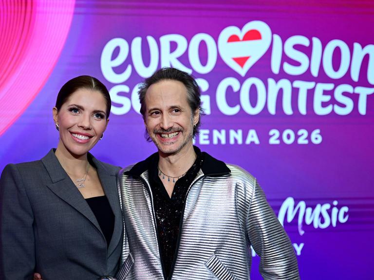 Die Moderatoren Victoria Swarovski und Michael Ostrowski stehen lächelnd vor einem Plakat mit der Aufschrift "eurovision song contest"