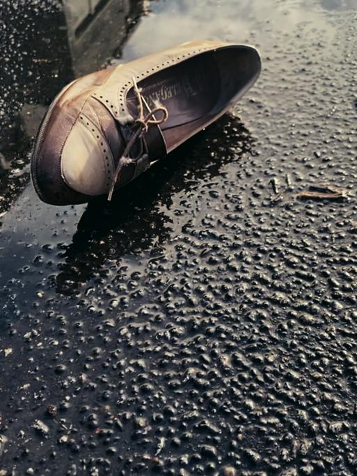 Szene aus Dominik Grafs Film "Jeder schreibt für sich allein": Ein Damenschuh liegt seitlich auf einer Straße neben einer Pfütze.