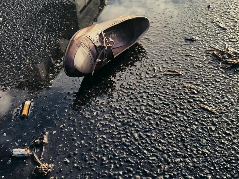 Szene aus Dominik Grafs Film "Jeder schreibt für sich allein": Ein Damenschuh liegt seitlich auf einer Straße neben einer Pfütze.