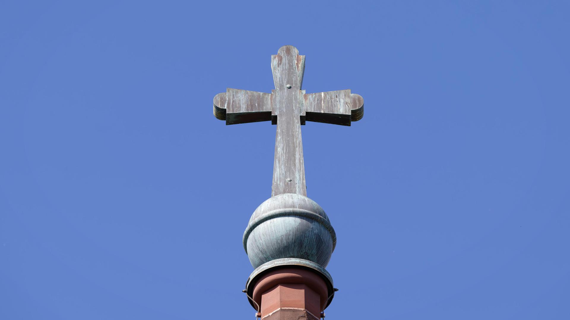 Architektonisches Detail des alten Kupferkreuzes mit Patina auf einem Kirchturm vor einem blauen Himmel.