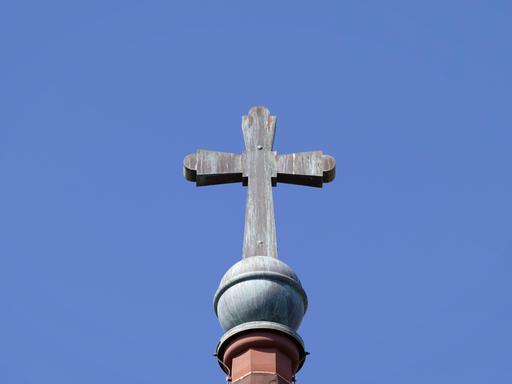 Architektonisches Detail des alten Kupferkreuzes mit Patina auf einem Kirchturm vor einem blauen Himmel.
