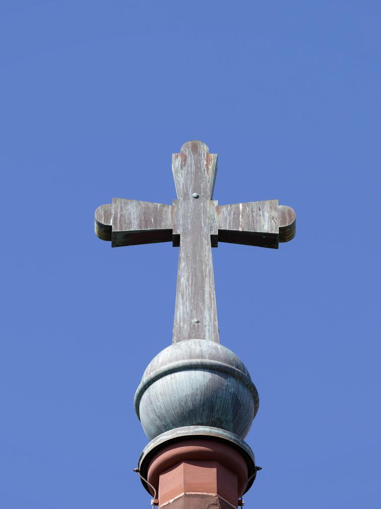 Architektonisches Detail des alten Kupferkreuzes mit Patina auf einem Kirchturm vor einem blauen Himmel.