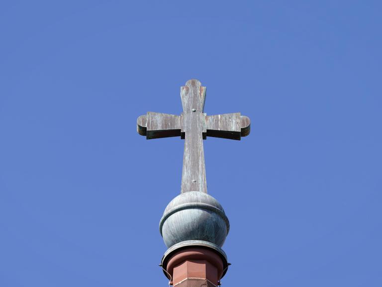 Architektonisches Detail des alten Kupferkreuzes mit Patina auf einem Kirchturm vor einem blauen Himmel.