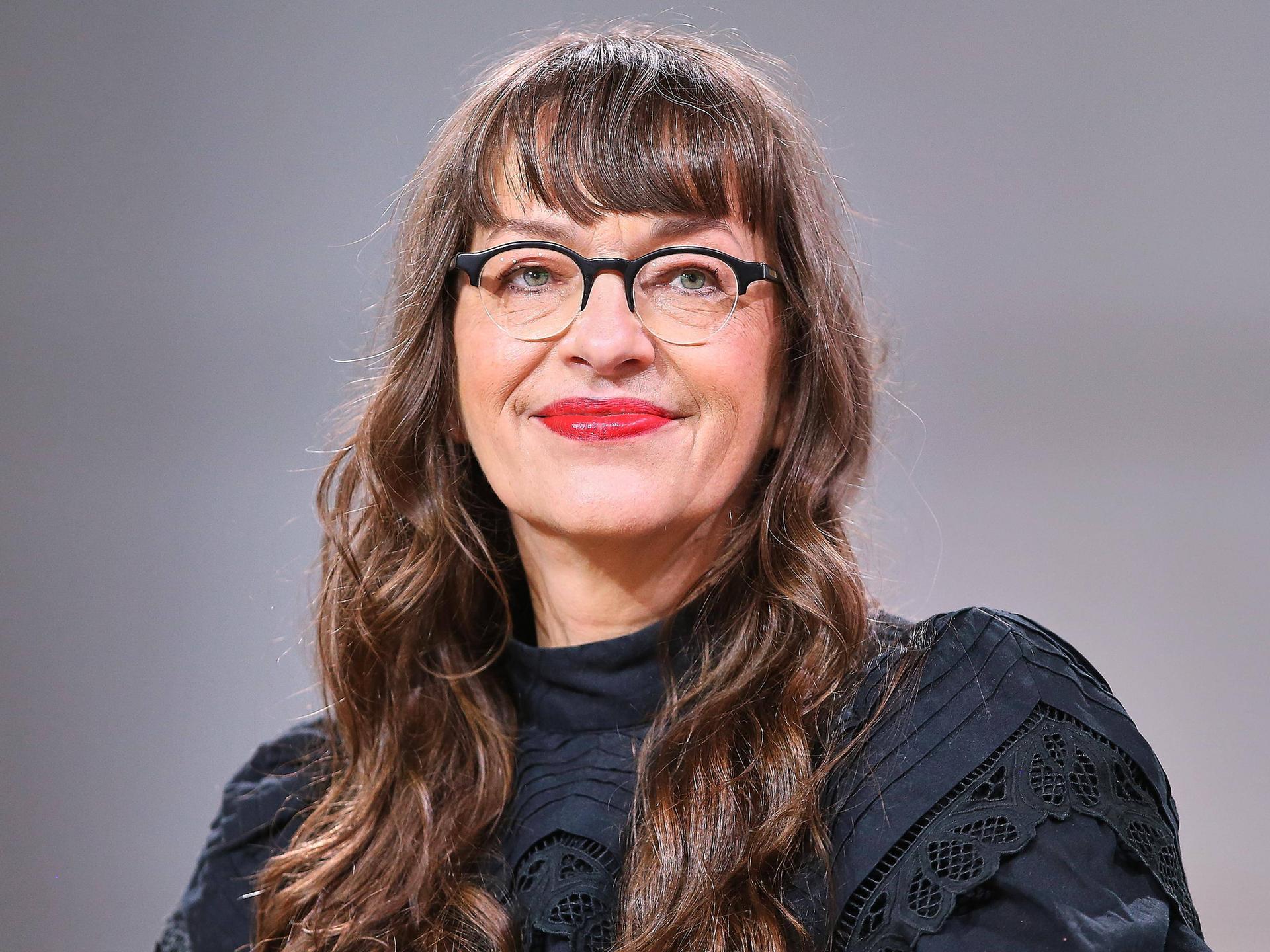 Ein weiße Frau mit Brille und langen braunen Haaren blickt in die Kamera.