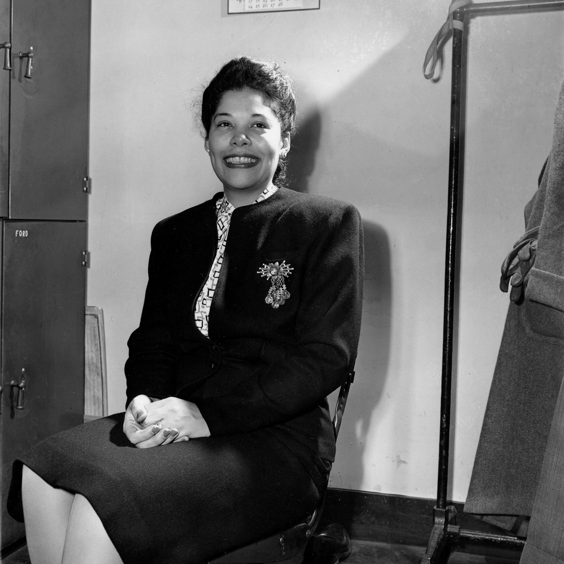 Die AUtorin Ann Petry, gekleidet in einen schwarzen Blazer und Rock sitzt auf einem Stuhl in New York City am 6. Februar 1946 und lächelt in die Kamera.