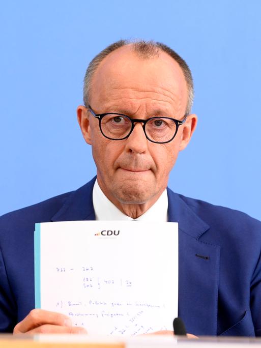 Foto zeigt Friedrich Merz bei der Bundespressekonferenz zu den Konsequenzen aus Solingen im Haus der Bundespressekonferenz in Berlin. Dabei hält er einen Notizettel mit dem Logo der CDU in den Händen.