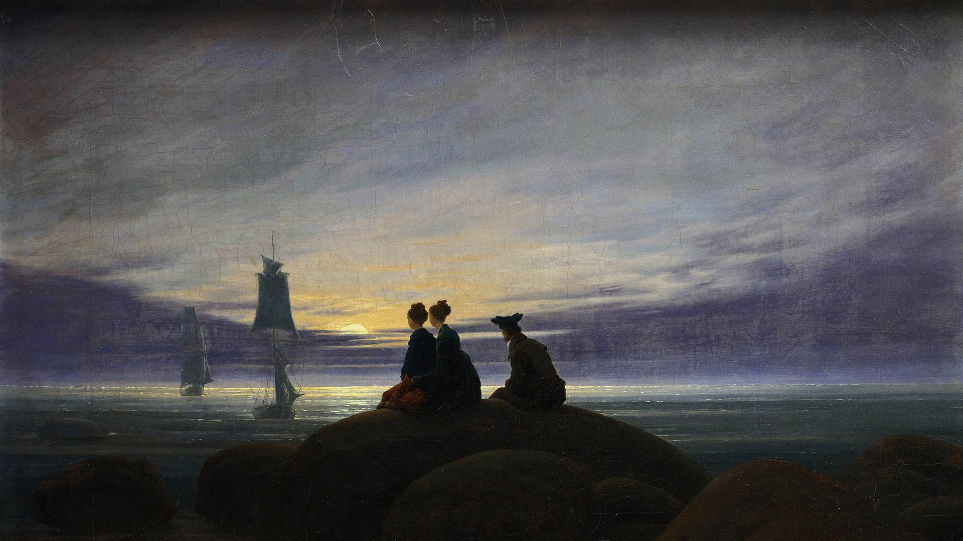 Digitale Reproduktion des Gemäldes Mondaufgang am Meer" (1822) von Caspar David Friedrich (1774 -1840). Zu sehen sind zwei Frauen und ein Mann, die auf einem Felsen im Mondschein sitzend auf in der Ostsee ankernde Segelschiffe schauen. 