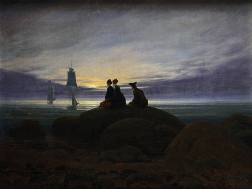 Digitale Reproduktion des Gemäldes Mondaufgang am Meer" (1822) von Caspar David Friedrich (1774 -1840). Zu sehen sind zwei Frauen und ein Mann, die auf einem Felsen im Mondschein sitzend auf in der Ostsee ankernde Segelschiffe schauen. 