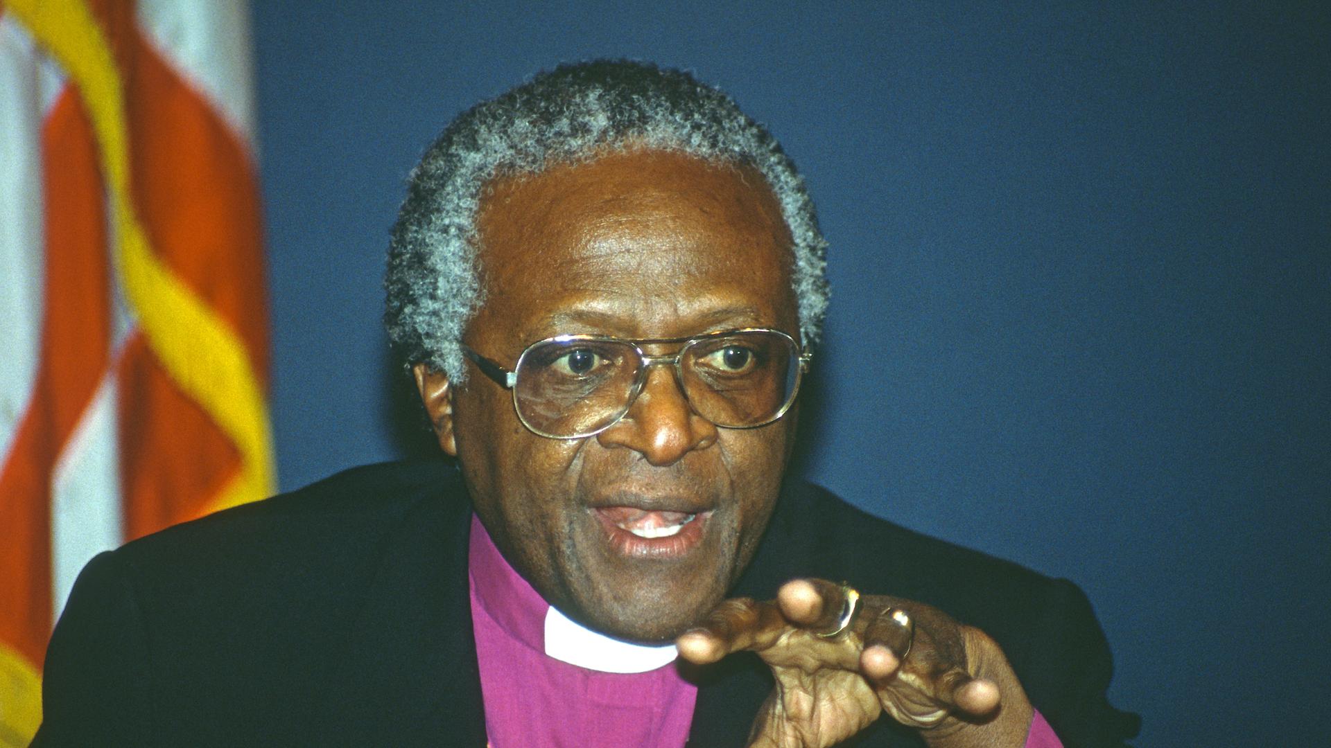 Der südafrikanische Erzbischof und Friedensnobelpreisträger Desmond Tutu gestikuliert in die Kamera. Er trägt lila Ornat unter dem Sakko. Der südafrikanische Erzbischof und Friedensnobelpreisträger Desmond Tutu gestikuliert in die Kamera. Er trägt lila Ornat unter dem Sakko.