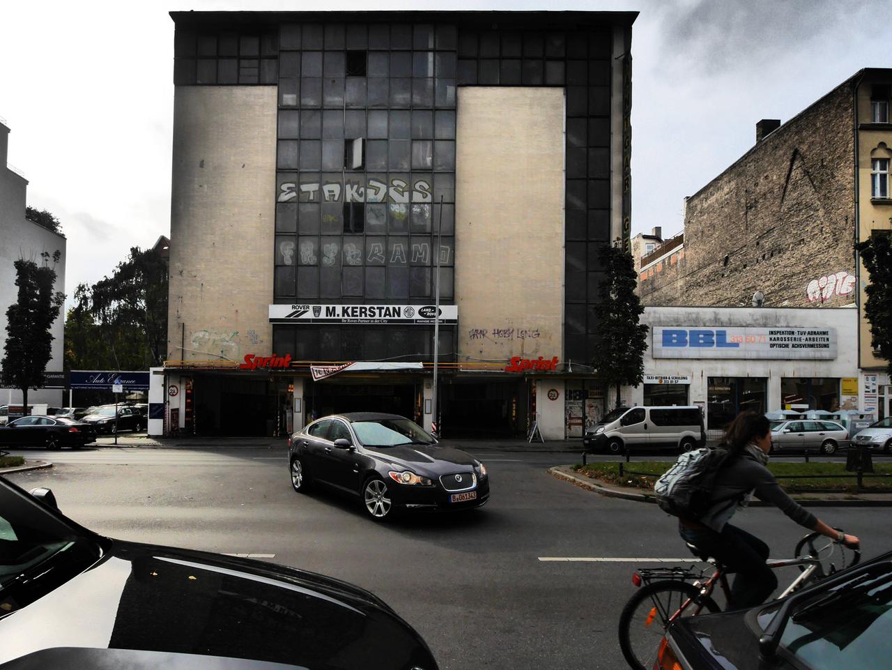 Ein Bild der Kant-Garage aus dem Jahr 2014. Der Putz des Gebäudes ist dunkelbesch, Graffiti ist auf dem Gemäuer. Auf dem Nachbargrundstück steht ein eingeschossiger Bau, vom nächsten Haus ist die Brandmauer zu sehen.