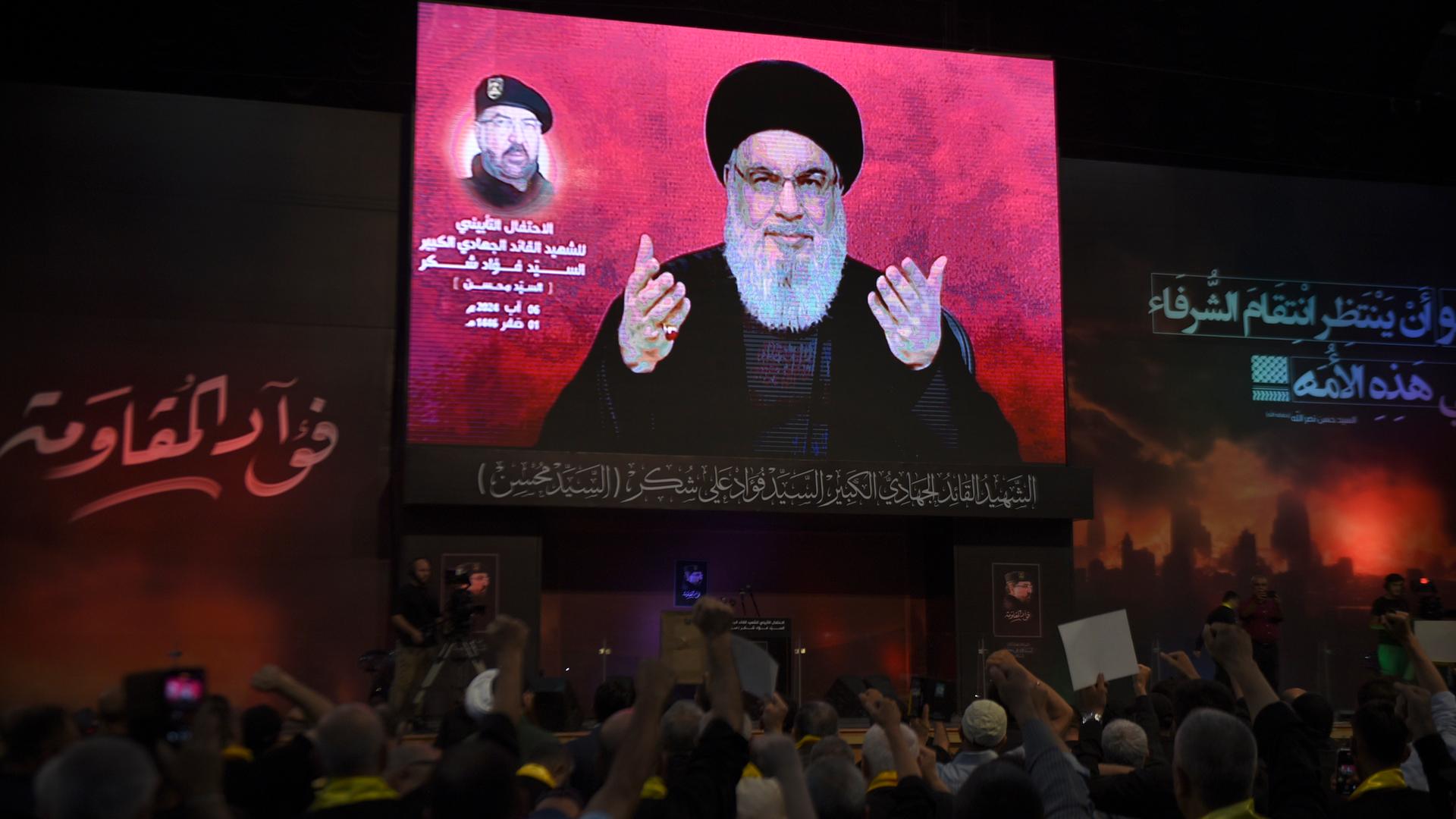 Beirut: Anhänger erheben ihre Fäuste und jubeln, während sie eine Rede des Hisbollah-Führers Nasrallah auf einem Bildschirm verfolgen, die während einer Zeremonie zum Gedenken an den Tod des obersten Befehlshabers Fouad Shukur, der letzte Woche durch einen israelischen Luftangriff getötet wurde, gehalten wird. 