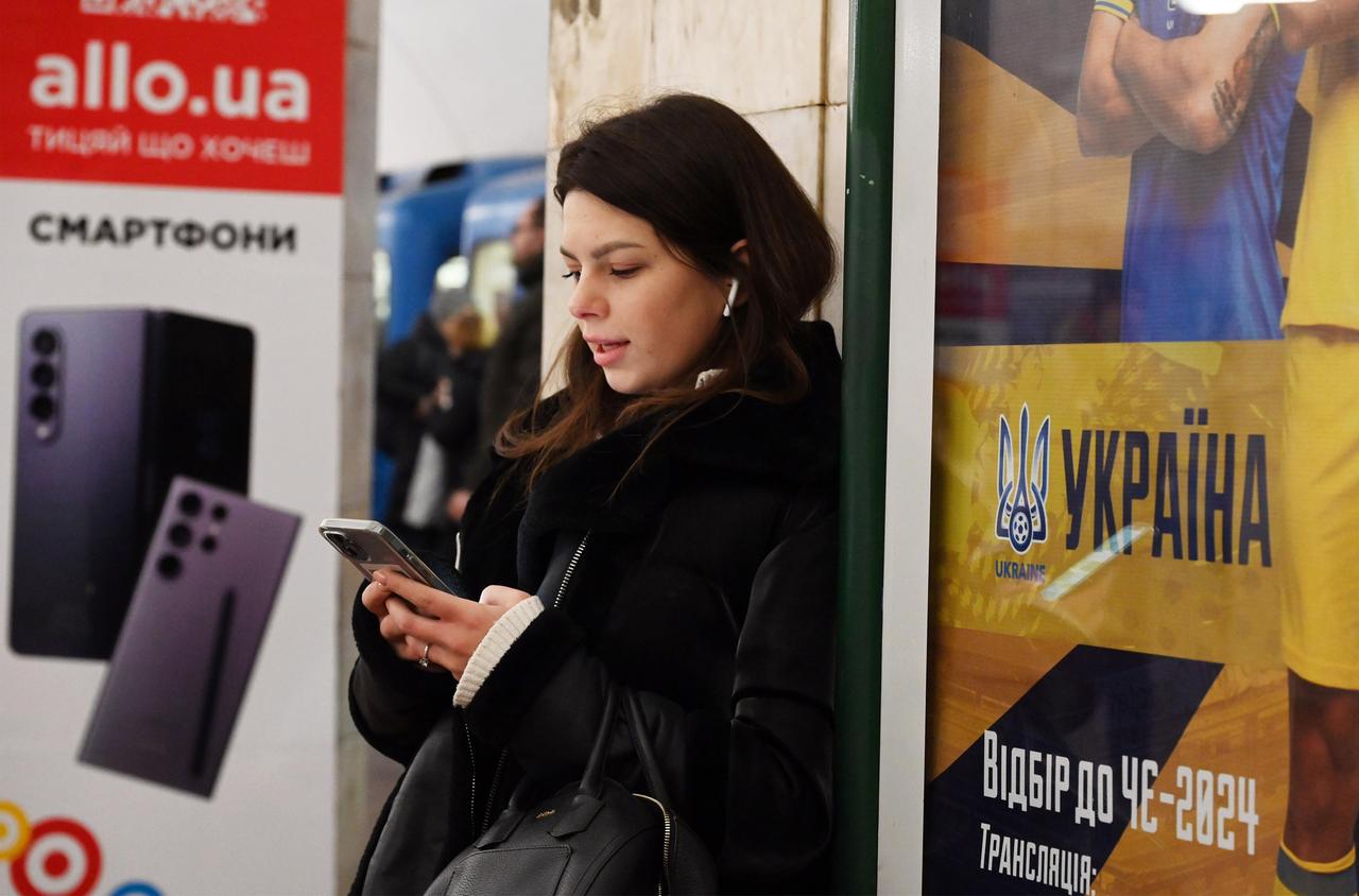 Eine junge Frau steht mit einem Handy in der Kiewer U-Bahn.