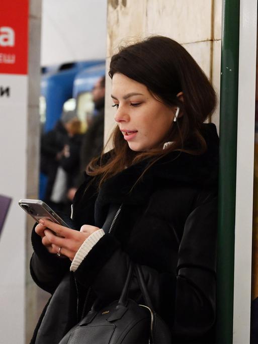 Eine junge Frau steht mit einem Handy in der Kiewer U-Bahn.