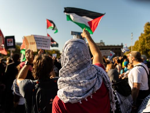 Person mit Palästinensertuch auf dem Kopf und Palästina-Flagge bei einer Demo in Berlin