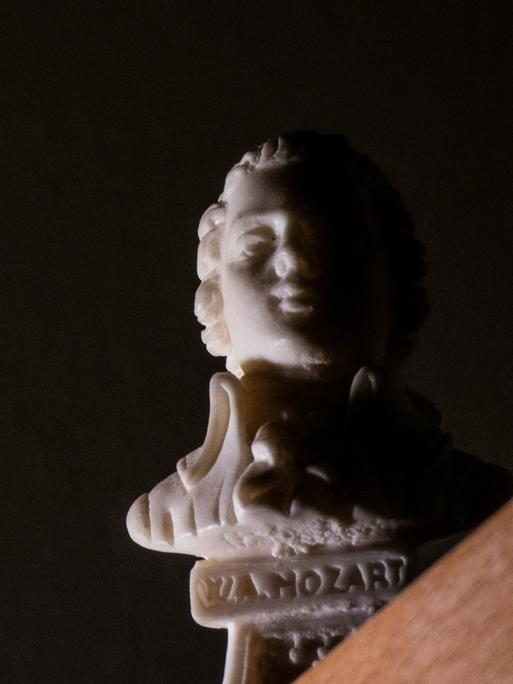 Blick auf eine kleine Mozart-Statue, die an einer Tischkante steht und nur von einer Seite beleuchtet wird.