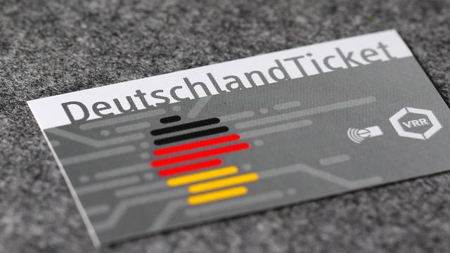 Eine Karte liegt auf einem Tisch. Darauf steht: Deutschland-Ticket. Es ist der Umriss von Deutschland zu sehen in den Farben schwarz, rot und gelb.