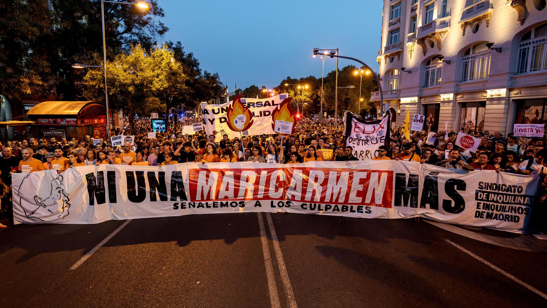 Auf einer Straße geht eine große Menschenmenge, die ein Transparent vor sich trägt. Darauf steht: "Ni una Maricarmen más".