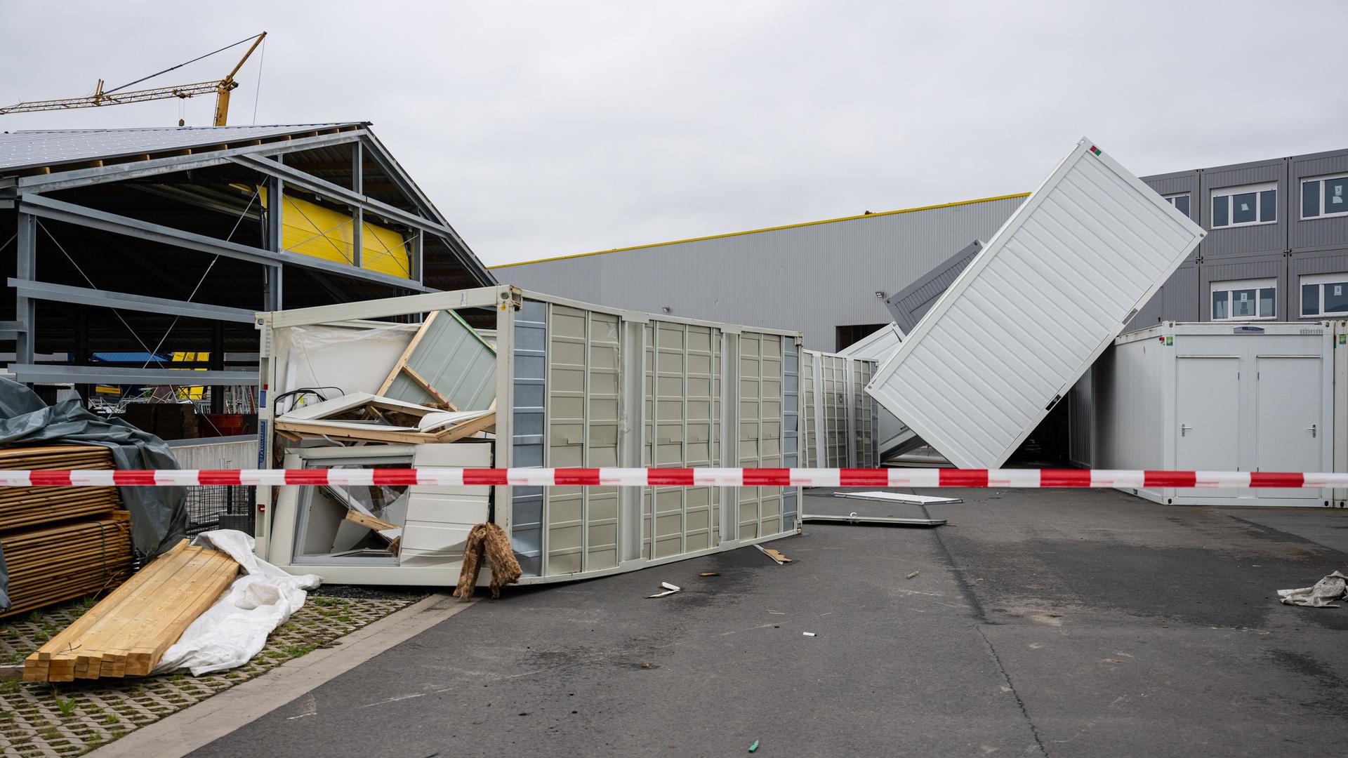 Auf dem Gelände einer Firma liegen nach einem heftigen Sturm umgestürzte Container auf dem Hof. Im Vordergrund ist ein rot-weißes Absperrband zu sehen. Auf dem Gelände einer Firma liegen nach einem heftigen Sturm umgestürzte Container auf dem Hof. Im Vordergrund ist ein rot-weißes Absperrband zu sehen.
