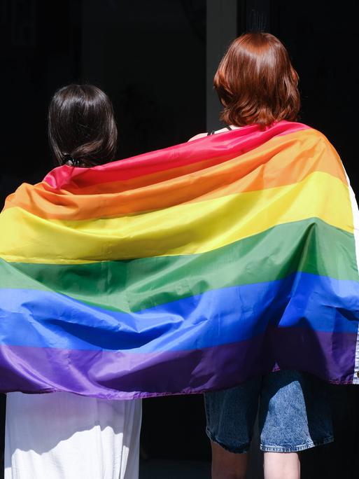 Zwei Frauen tragen auf einem CSD eine Regen-Bogen-Fahne.