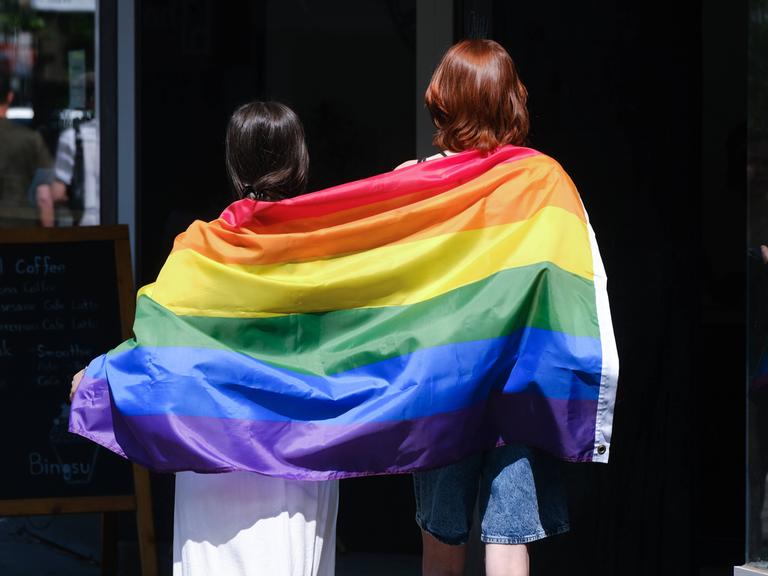 Zwei Frauen tragen auf einem CSD eine Regen-Bogen-Fahne.
