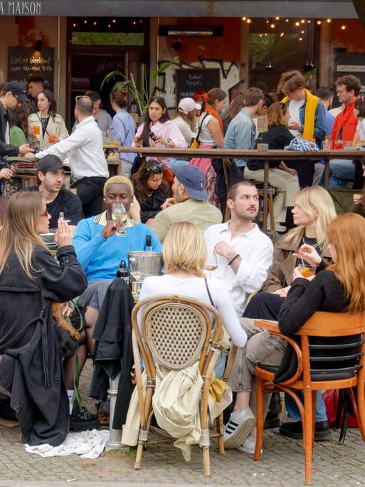 Viele junge Leute sitzen auf der Terrasse eines Cafés.