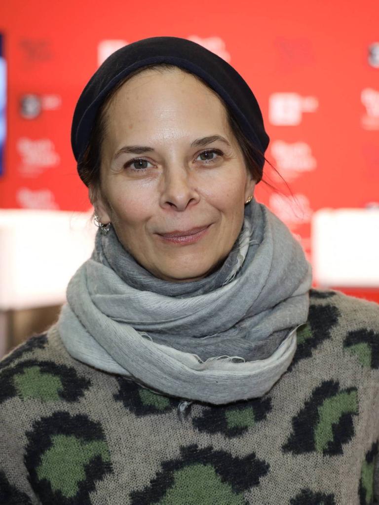 Anna Baar trägt eine schwarze Mütze und graue Kleidung und steht vor einem roten Hintergrund.