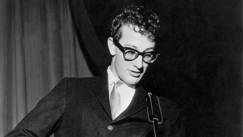 Buddy Holly bei einem Konzert Ende der 50er-Jahre. Er trägt seine berühmte schwarze Hornbrille, Anzug und Krawatte.
