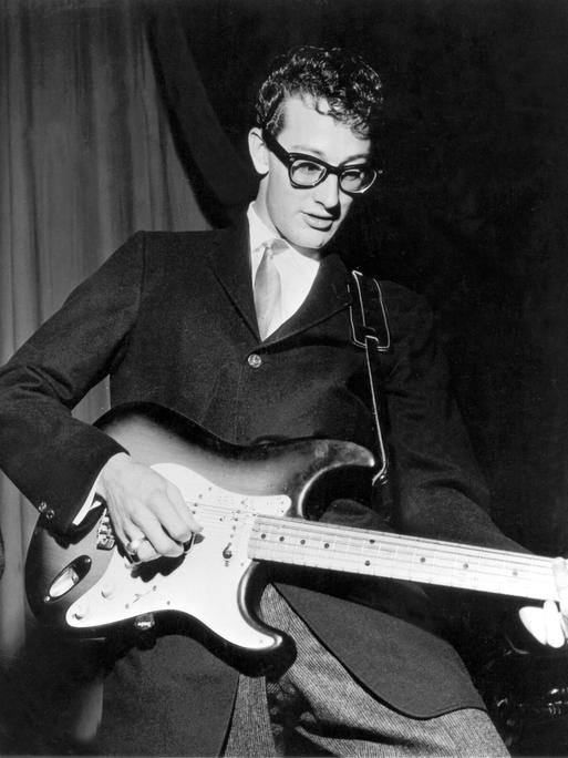 Buddy Holly bei einem Konzert Ende der 50er-Jahre. Er trägt seine berühmte schwarze Hornbrille, Anzug und Krawatte.