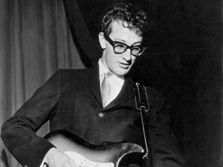 Buddy Holly bei einem Konzert Ende der 50er-Jahre. Er trägt seine berühmte schwarze Hornbrille, Anzug und Krawatte.