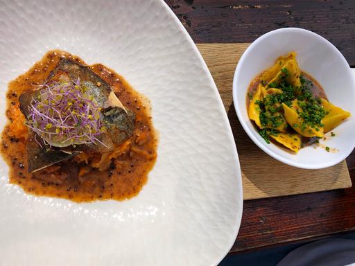 Gebratene Forellenfilets und bayrisches Kim Chi mit Teigtaschen und Sesam sind in zwei weißen Tellern angerichtet