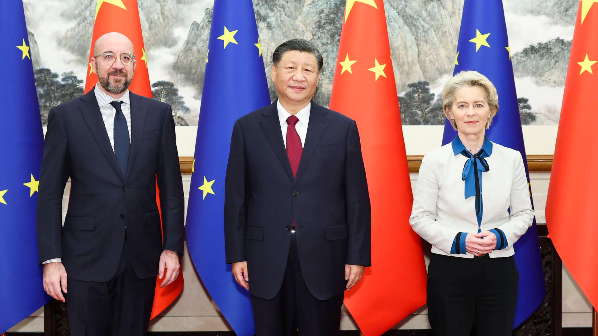 EU-Ratspräsident Michel, Chinas Präsident Xi und EU-Kommissionspräsidentin von der Leyen stehen nebeneinander vor EU- und China-Flaggen.