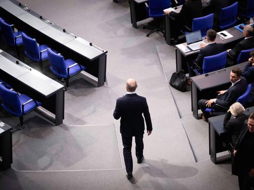 Olaf Scholz während der Debatte bei einer Sitzung des Deutschen Bundestages. Man sieht ihn von hinten durch die Reihen laufen. 