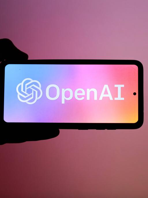 Das Logo von "OpenAI" auf einem Smartphone vor einem dunkelrosa-farbenen Hintergrund