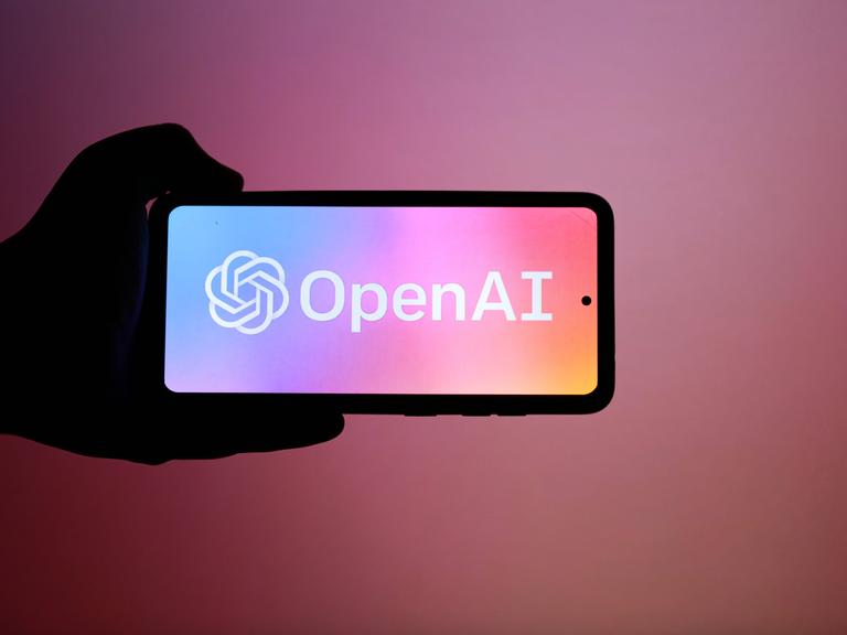 Das Logo von "OpenAI" auf einem Smartphone vor einem dunkelrosa-farbenen Hintergrund