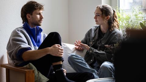 Die Geschwister Emmanuel und Maria Gottschalk unterhalten sich auf einer Couch in der Wohnung des Bruders.