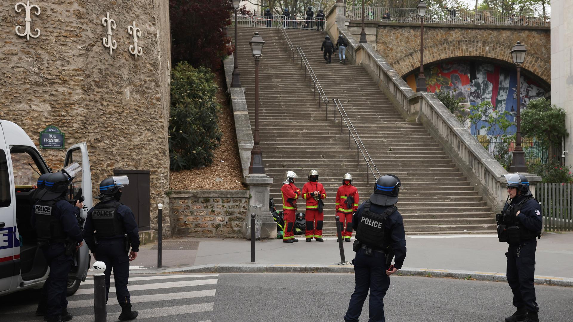 Polizisten und Rettungskräfte warten vor dem iranischen Konsulat in Paris. Sie sind in ihren Uniformen von hinten zu sehen.