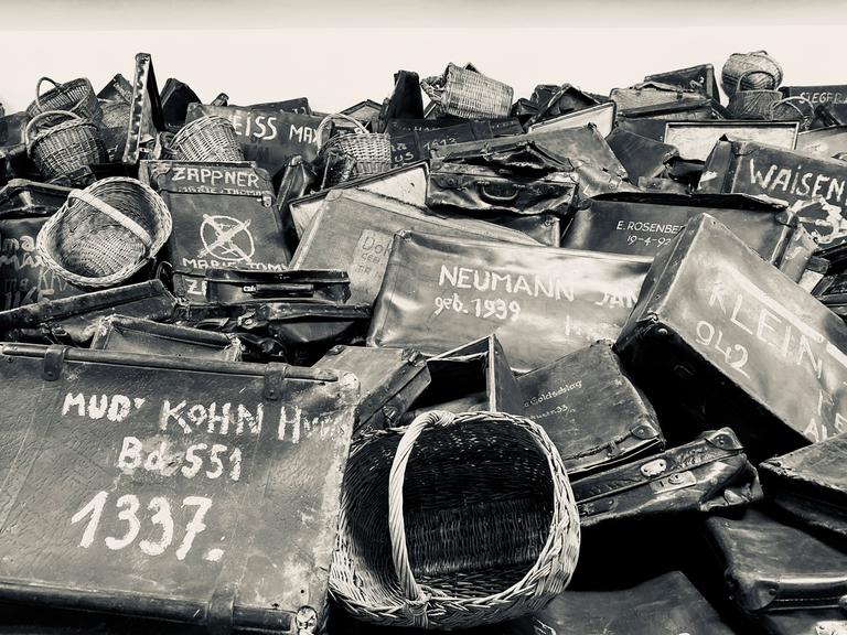 Schwarzweißfoto eines Haufens mit Koffern von Insassen des Konzentrationslagers Auschwitz. Die Namen der Insassen stehen in großen, weißen Buchstaben auf den Koffern.