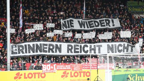 Zuschauer halten beim Fußball-Bundesligaspiel SC Freiburg gegen 1899 Hoffenheimbeim im Freiburger Schwarzwaldstadion Plakate mit der Aufschrift "Nie wieder! Erinnern reicht nicht"  in die Höhe.