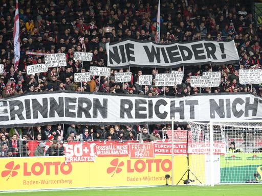 Zuschauer halten beim Fußball-Bundesligaspiel SC Freiburg gegen 1899 Hoffenheimbeim im Freiburger Schwarzwaldstadion Plakate mit der Aufschrift "Nie wieder! Erinnern reicht nicht"  in die Höhe.