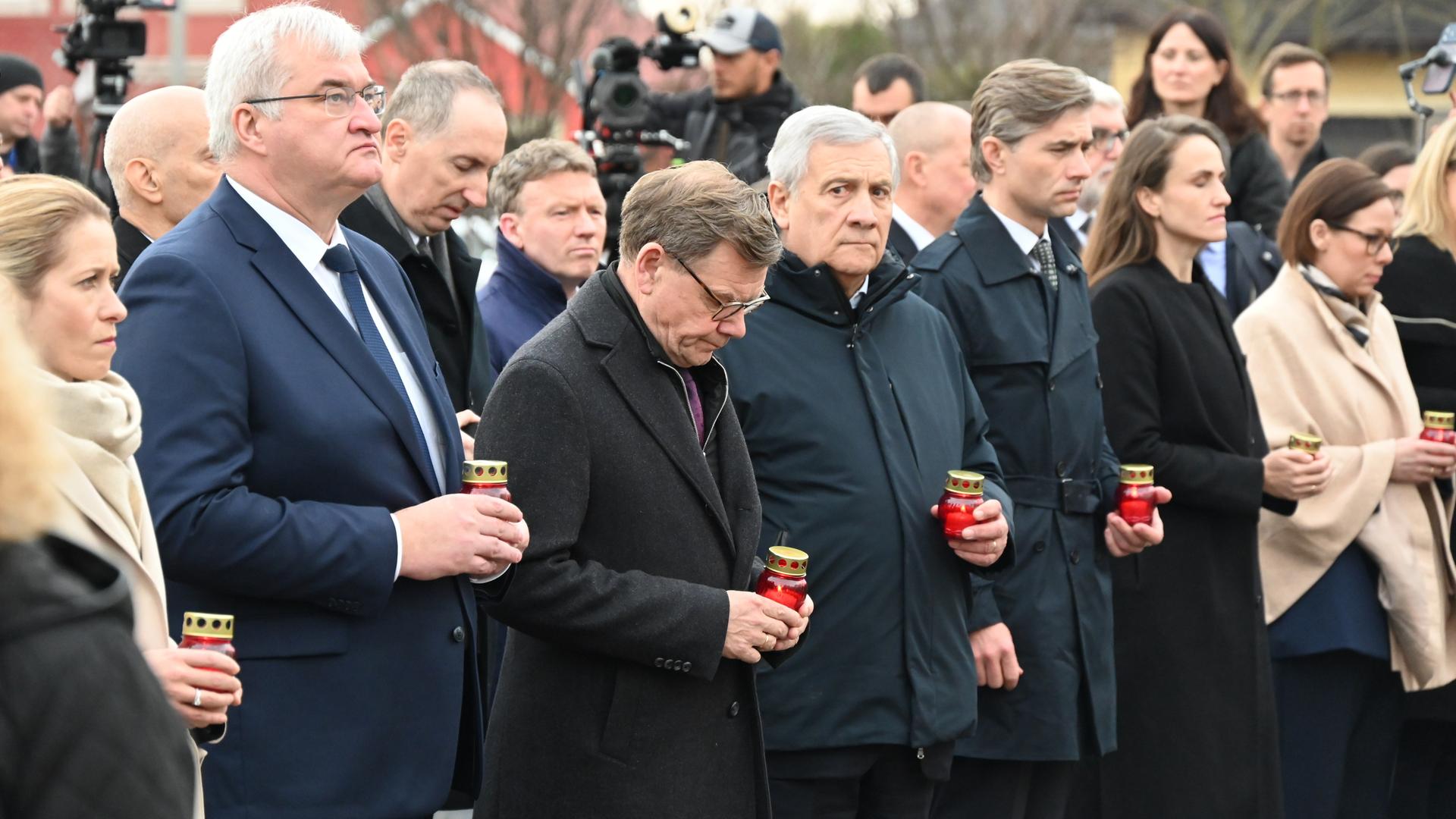 Mehrere Außenminister der EU-Staaten gedenken der Opfer in Butscha. Die Politiker halten Kerzen in den Händen. 