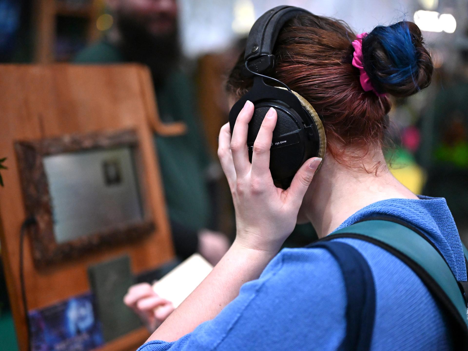 Eine Frau lauscht mit großen Kopfhörern auf dem Kopf einem Hörbuch auf der Leipziger Buchmesse. Man sieht sie von der Seite. 
