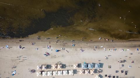 Jumala Beach in der Nühe von Riga an der lettischen Ostseeküste von oben. Am Strand sind einige Menschen und Sonnenschirme zu erkennen.