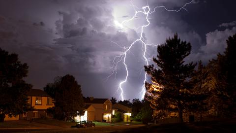 Über einem Wohngebiet steht eine Gewitterwolke, aus der ein weit verzweigter Blitz hervorschlägt.