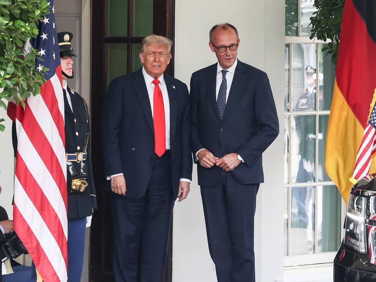 US-Präsident Donald Trump und Bundeskanzler Friedrich Merz nebeneinander vor dem Weißen Haus, neben ihnen sind die amerikanische und die deutsche Flagge gehisst.
